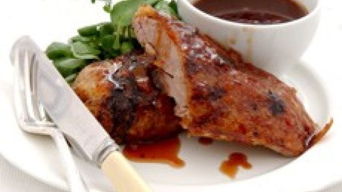cooked duck on a white plate with seville orange sauce poured over the top, a little white bowl of sauce on one side and a knife and fork on the other