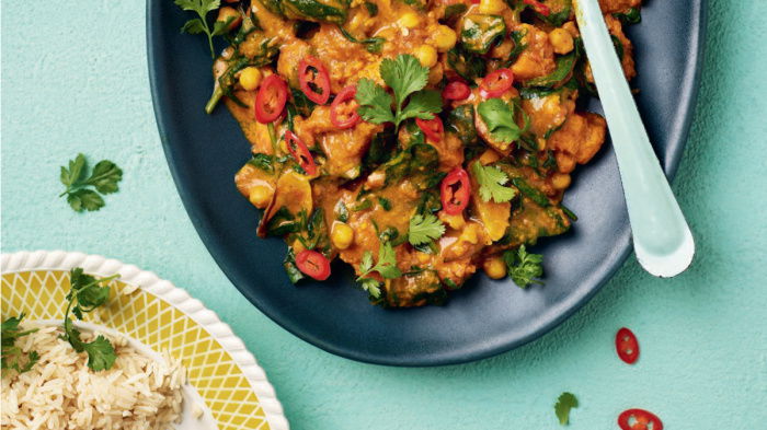 a colourful picture of a black dish with chickpea curry garnished with coriander, and a dish of cooked rice next to it