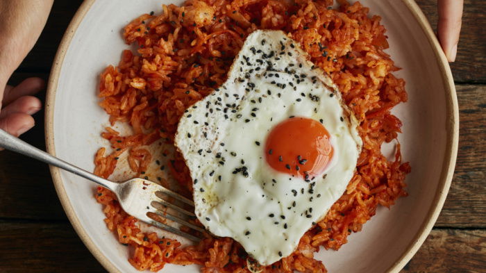 a picture of a bowl of kimchi fried rice sitting on a wooden table top