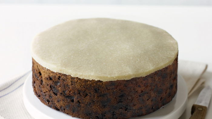 a Picture of a fruit cake on a white plate with a layer of marzipan on th top