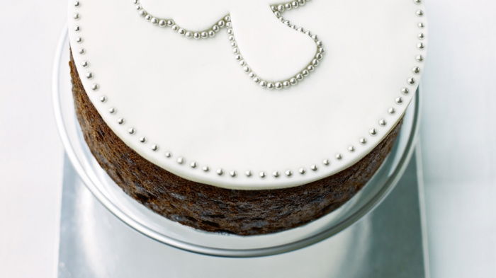 a picture of a cooked cake on a silver cake board, with white icing and an angel marked out in little silver balls