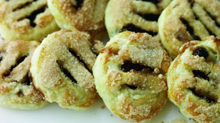 A picture of a batch of cooked eccles cakes, all lined up overlapping each other