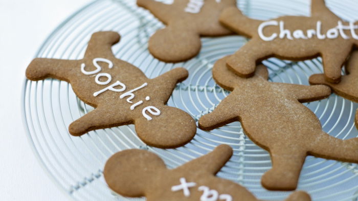 Five little gingerbread men lying on a circular wire tray four of them with the names Tom, Sophie, Max and Charlotte iced on their tummies