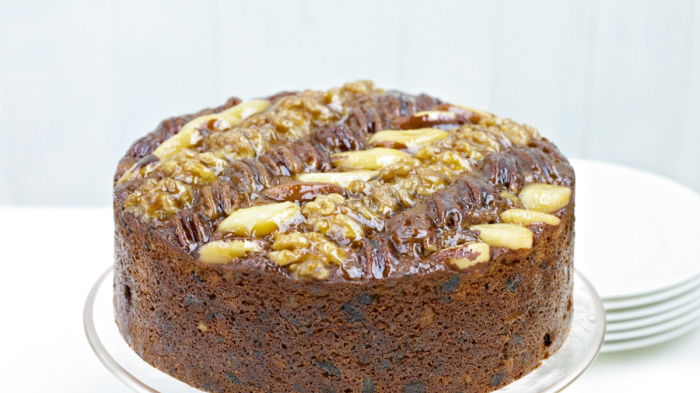 A picture of a fruit cake decorated with nuts on the top on a white cake stand