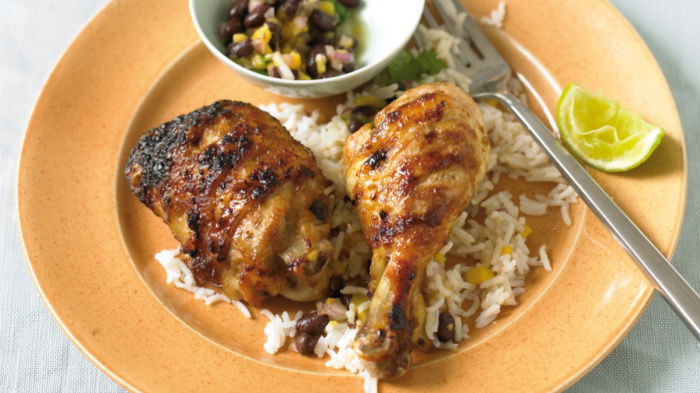 a yellow plate of cooked chicken and rice with a wedge of lemon on the edge