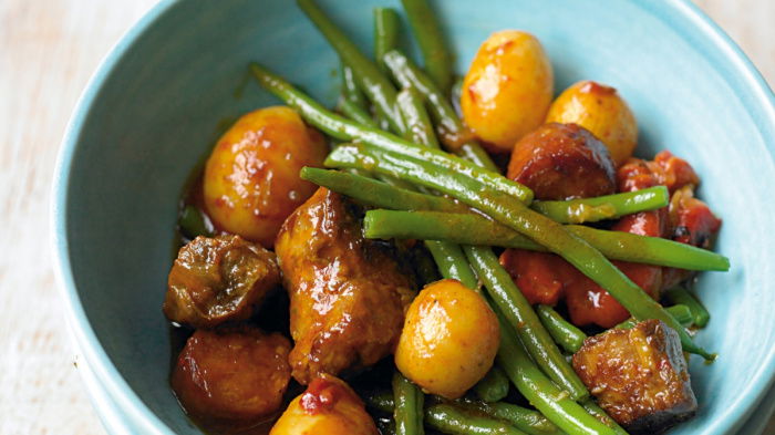 A picture of cooked pork stew with green beans and potatoes in a blue bowl