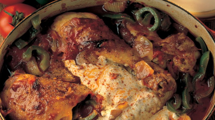 A round oven dish of cooked chicken paprika with green peppers and soured cream on the top