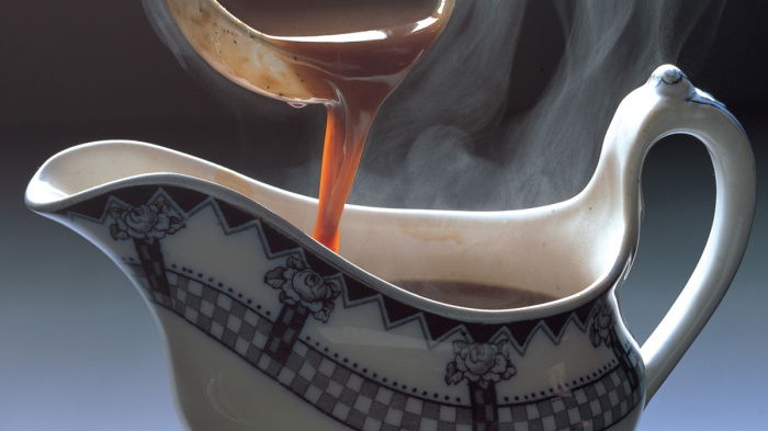 A blue and white china gravy boat with gravy being poured in from a ladle above it