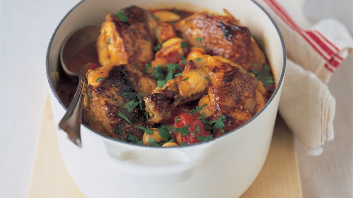 a picture of a white casserole dish with cooked chicken butter beans chorizo and tomatoes with a spoon resting on the side