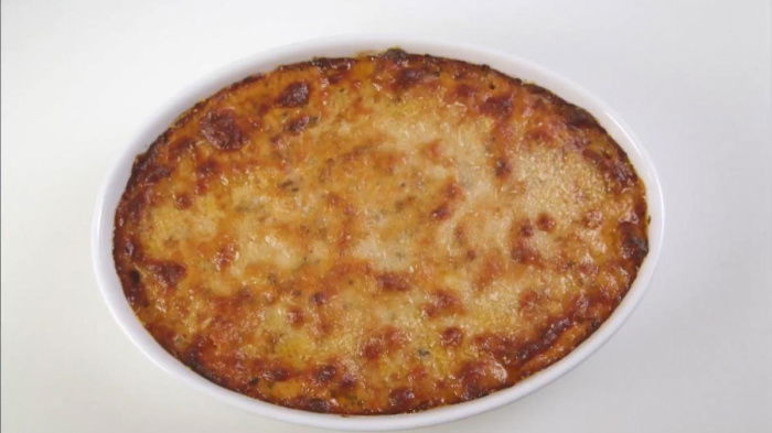 An oval white dish containing baked pasta with cheese browned on the top