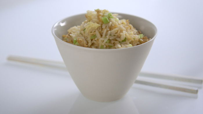 a white bowl containing stirfried rice, with two white chopsticks next to it