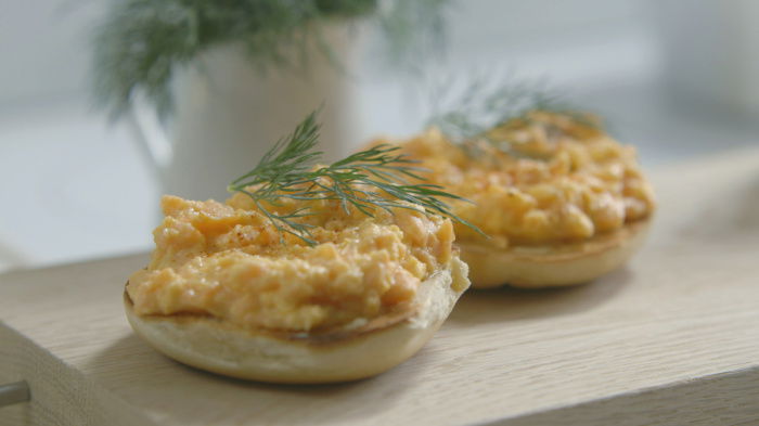 a picture of a bagel cut in half with scrambled egg and a garnish of dill on top 
