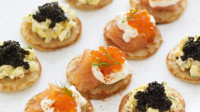 a picture of a white plate of little blinis with smoked salmon and caviar on the top