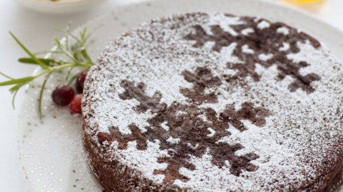 a picture of a chocolate cake with sknowflakes marked out with icing sugar, on a white plate