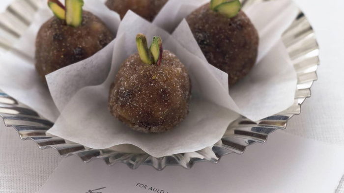 A picture of four sugared plums in paper cases on a silver plate with the words to auld lang syne on a sheet of paper