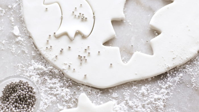 a picture of a circular sheet of white fondant icing on a white surface. three shooting stars have been cut out, a little dish of silver balls alongside and icing sugar on the top