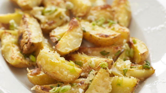 a white dish containing thick wedges of potatoes with cheese sprinkled on the top