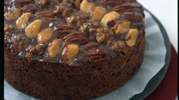 A picture of a round fruit cake decorated with nuts on the top on a dark plate
