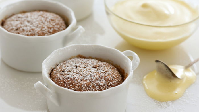 Three little white dishes on a white plate, with souffles dusted with icing sugar and a glass bowl of sabayon on the side