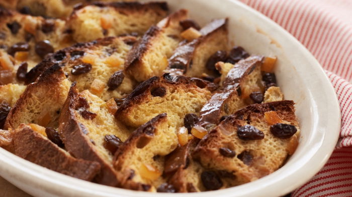 Slices of panettone bread layered in a white oval bowl with a red and white napkin next to it on a wooden board