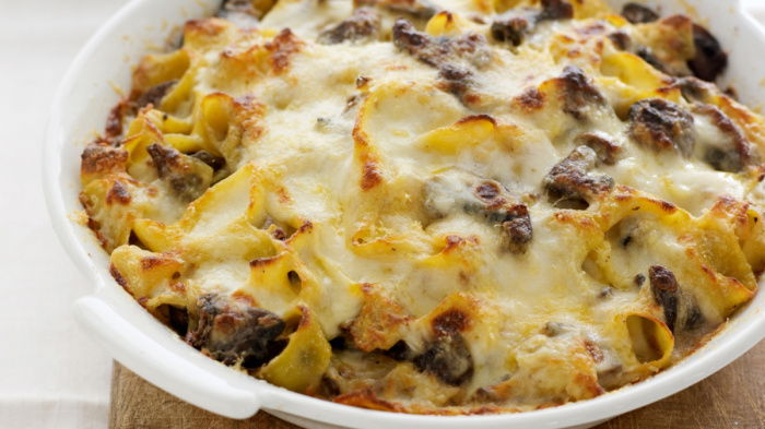 A white oven proof dish of a baked pasta dish with melted cheese on the top