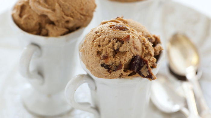 three pretty white dishes of ice cream on a white plate with spoons resting by the side