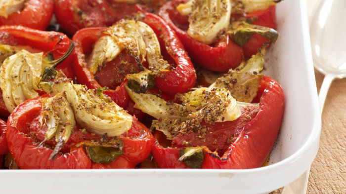 cooked red peppers and fennel in a white serving dish on a wooden serving board