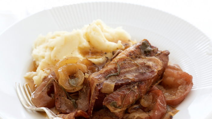 A picture of braised belly pork with bacon apples and cider on a white plate