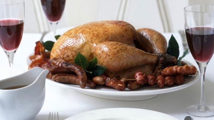 a picture of a table set with white plates, cutlery wine glasses and a cooked turkey with all the trimmings
