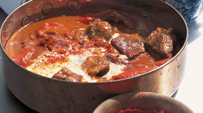 Braised beef goulash in a copper tin with a little bowl of smoked pimenton next to it and a little blue and white jug