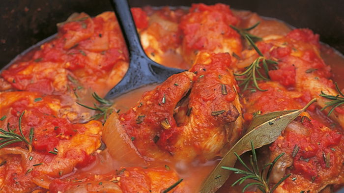 a pan of cooked chicken cacciatora with chicken thighs, rosemary and a tomatoey sauce