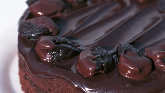a picture of a round chocolate sponge cake on a white plate with chocolate covered prunes decorating the top