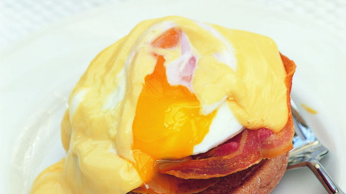 A white plate served with eggs benedict on top and a broken yolk