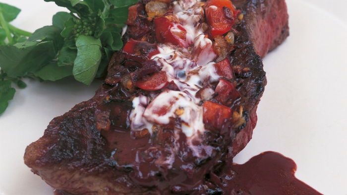 A picture of a cooked steak on. a white plate with sauce poured over the top and a watercress garnish on the side