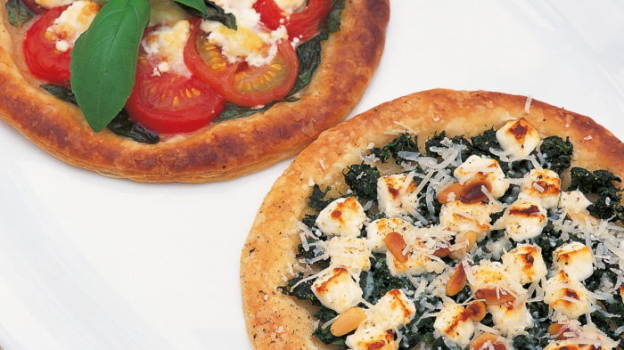 a pictue of two circular galettes, one with tomatoes goats cheese and basil and one with spinach and feta