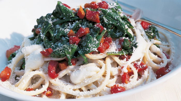 a white bowl of linguine with a gorgonzola sauce, cubes of mozarella, spinach, bacon and parmesan on top 