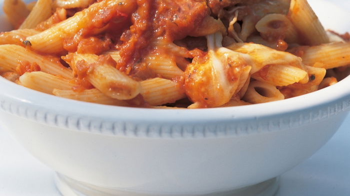 a close up of a white bowl filled with pasta and tomato sauce with basil leaves on the top
