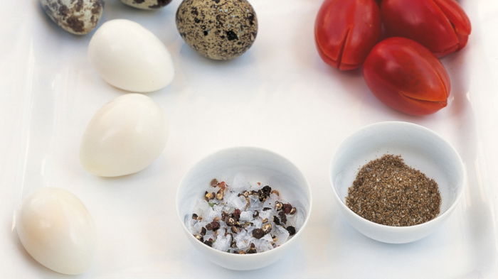 a picture of a white plate with quails eggs, tomatoes and two white dishes of salt