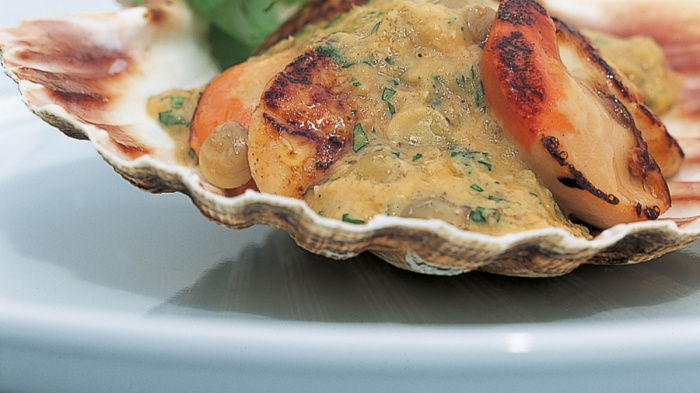 a pictur eof cooked scallops in a shell with lentils sauce and parsely garnish on the top