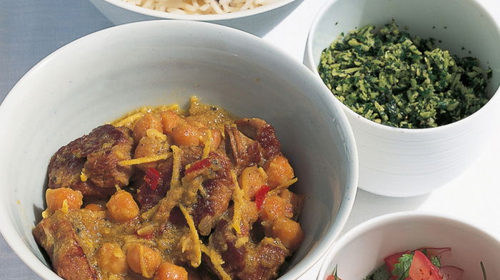 a picutre of four white dishes containing curry, rice, pickle and  sambal