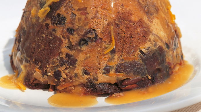 A Steamed Panettone Pudding with Eliza Acton's Hot Punch Sauce turned out on to a white plate with sauce dripping down the outside