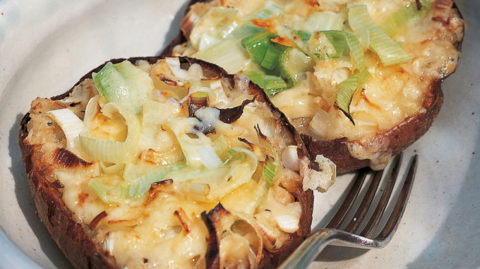 a picture of a cooked jacket potato cut in half and filled with melted cheese and leeks, resting on a plate