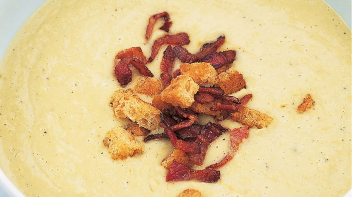 a white bowl of split pea soup garnished with crispy bacon and croutons