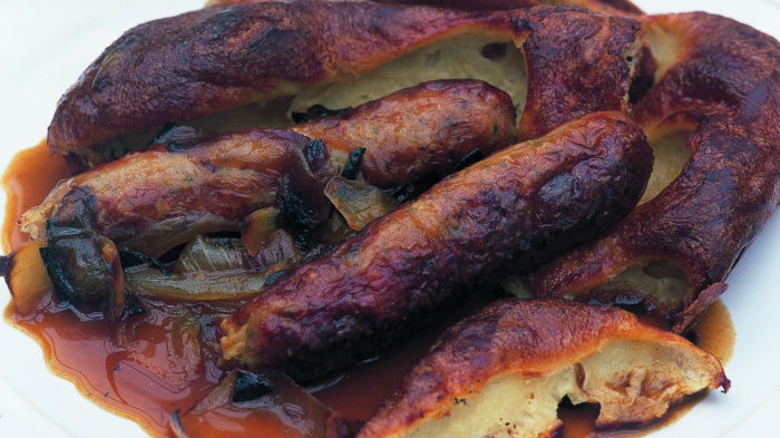 A white plate with cooked sausages batter and onion gravy