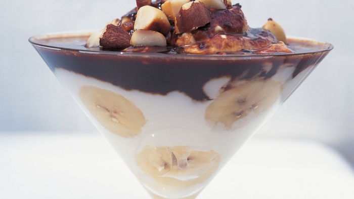 a glass sundae dish with greek yoghurt, bananas and chocolate in layers