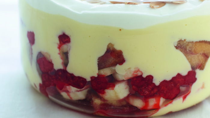 A picture of a glass bowl layered with sponge, fruit custard and cream making a trifle