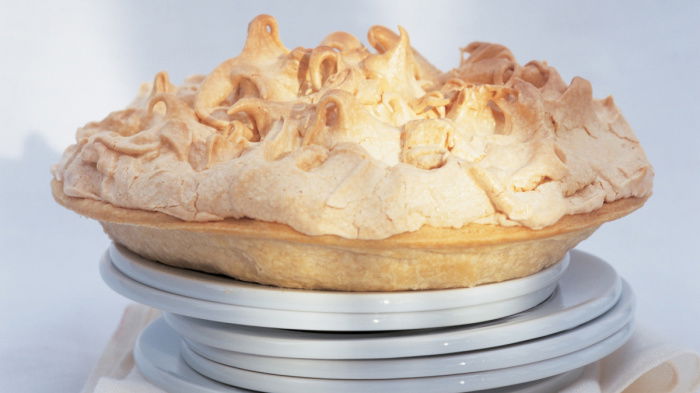 six white plates with a cooked lemon meringe pie balanced on the top