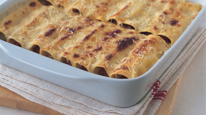 A square white dish with pasta sheets filled and rolled with the ragu sauce and parmesan cheese grated on the top