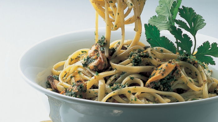a blue bowl filled with linguine pasta with mussels and walnut parsley pesto