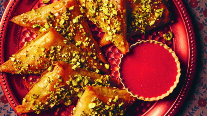 A picture of a red plate with samsas and a little bowl of strawberry coulis on the side